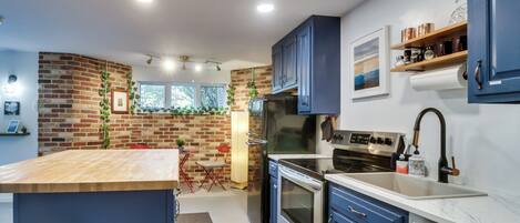 A modern kitchen with a brick wall, stainless steel appliances, and blue cabinets.