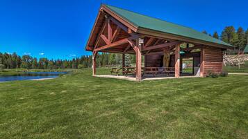 A wooden cabin with a green roof, situated on a grassy field with a lake in the background.