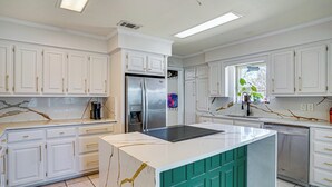 A modern kitchen with white cabinetry, a stainless steel refrigerator, and a central island with a green accent. - Private Beach & Dock: Home on Eagle Mountain Lake (Azle)