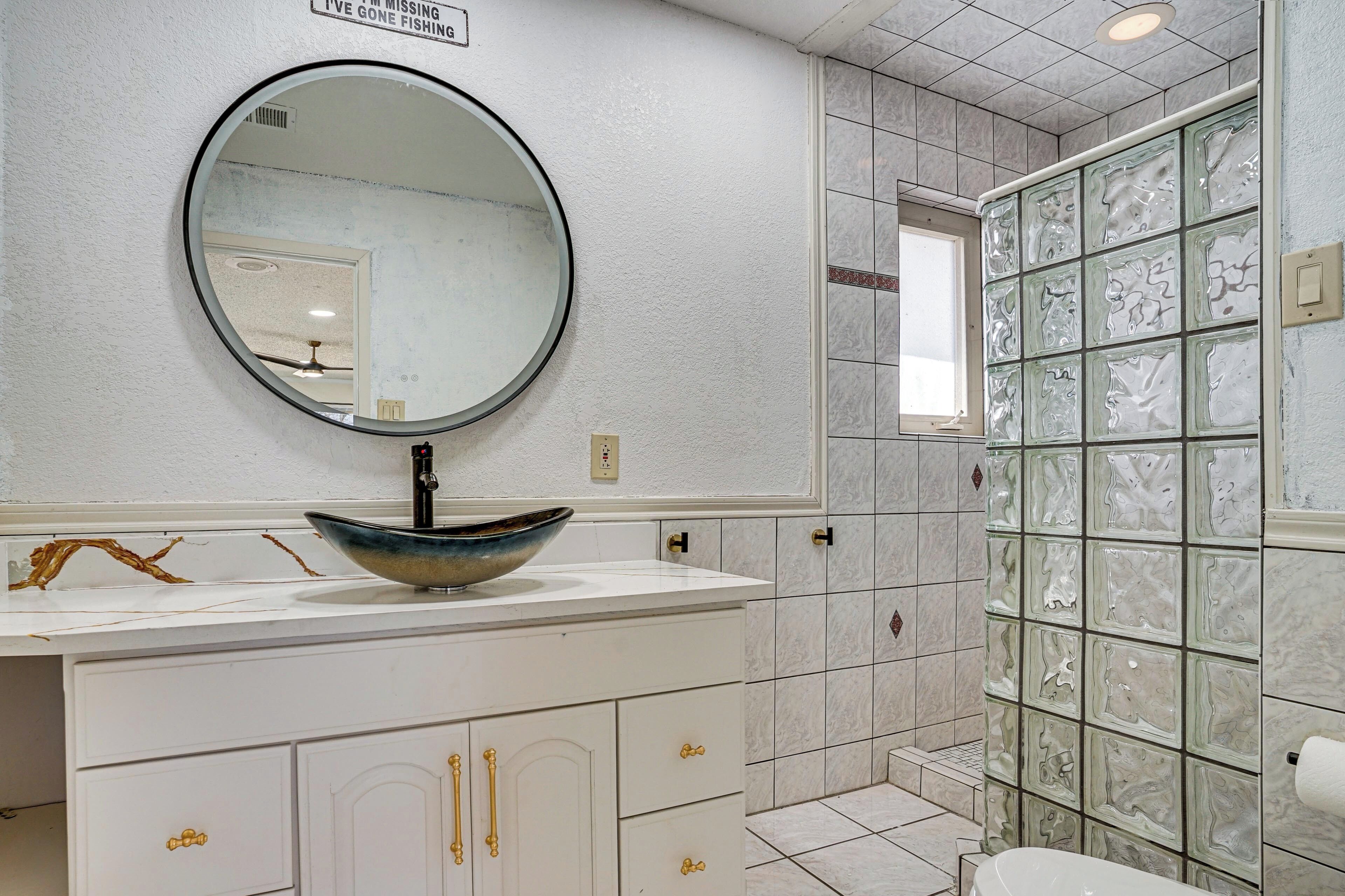 Een badkamer met een ronde spiegel, een wit wastafelmeubel met een blauwe wasbak en een douchecabine van glas.