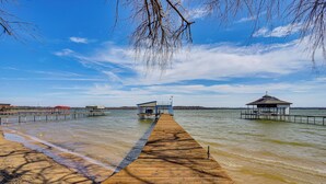 A wooden pier extending into a body of water with two buildings at the end. - Private Beach & Dock: Home on Eagle Mountain Lake (Azle)