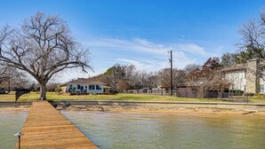 A wooden dock extending into a body of water with a house and trees in the background. - Private Beach & Dock: Home on Eagle Mountain Lake (Azle)