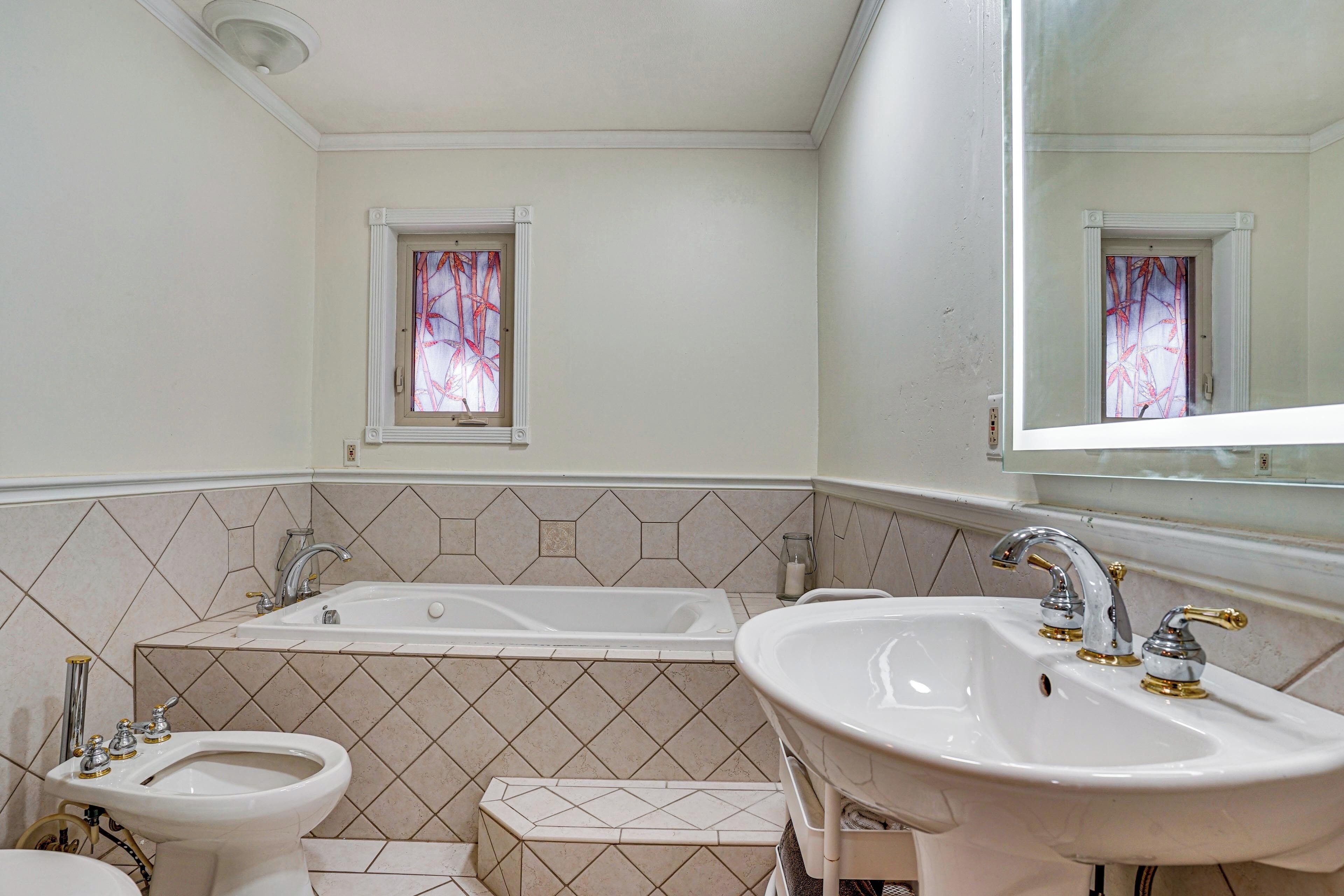 A bathroom with a bathtub, two sinks, and a window with a decorative view.