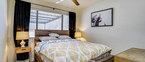 A bedroom with a wooden bed, a ceiling fan, a bedside table with a lamp, and a framed picture on the wall.