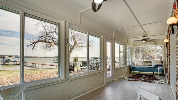 A spacious room with large windows overlooking a dock and water, a cozy seating area with a sofa and chairs, and a ceiling fan. - Private Beach & Dock: Home on Eagle Mountain Lake (Azle)