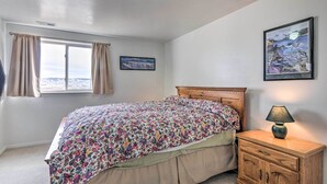 A bedroom with a bed, a nightstand, a lamp, a window with curtains, and two framed pictures on the wall.