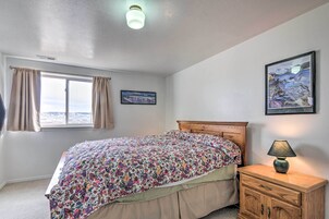 Un dormitorio con cama, mesita de noche, lámpara, ventana con cortinas y dos cuadros en la pared.