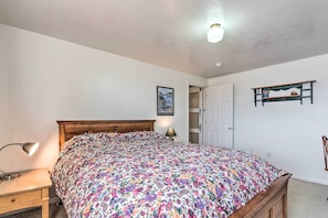 A bedroom with a wooden bed, a nightstand with a lamp, a door, and a shelf with decorative items.