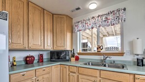 A kitchen with wooden cabinets, a microwave, a sink, and a window with a curtain.