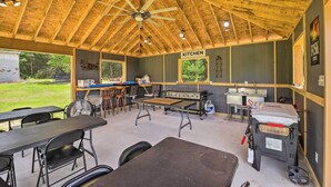 A covered outdoor kitchen area with tables, chairs, a ceiling fan, and a grill. - Stylish Woodville Cabin: Fishing Dock Access! (Woodville)