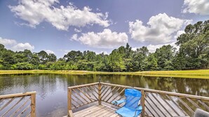 A wooden deck with a blue chair and a grey chair, overlooking a calm lake surrounded by trees. - Stylish Woodville Cabin: Fishing Dock Access! (Woodville)