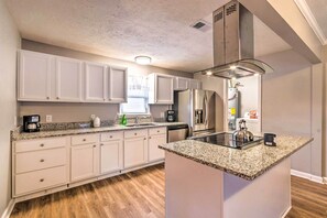 A modern kitchen with white cabinets, granite countertops, a stainless steel refrigerator, and a built-in oven. - Vacation Rental Home ~ 15 Mi to Little Rock (Jacksonville)