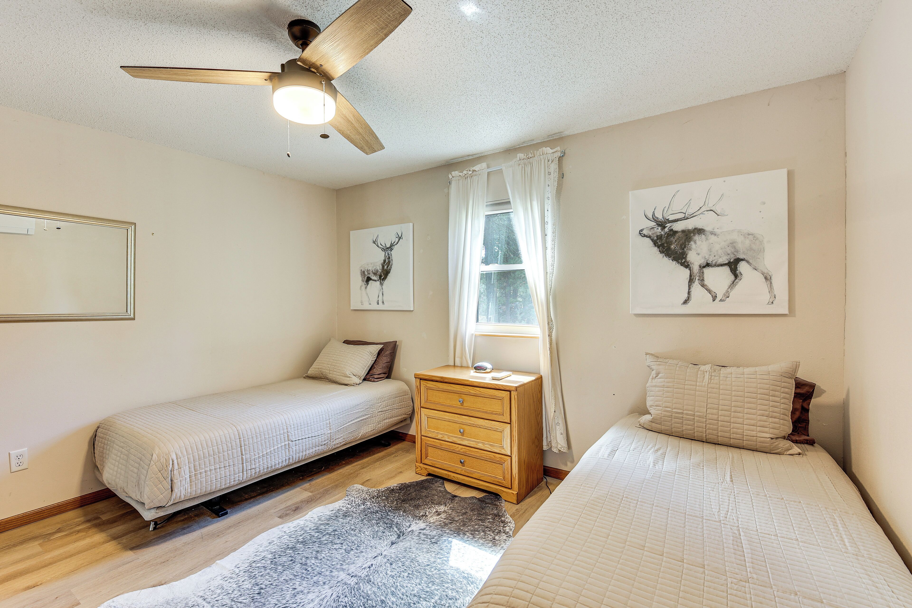 A bedroom with two beds, a wooden dresser, a ceiling fan, and artwork of deer on the walls.