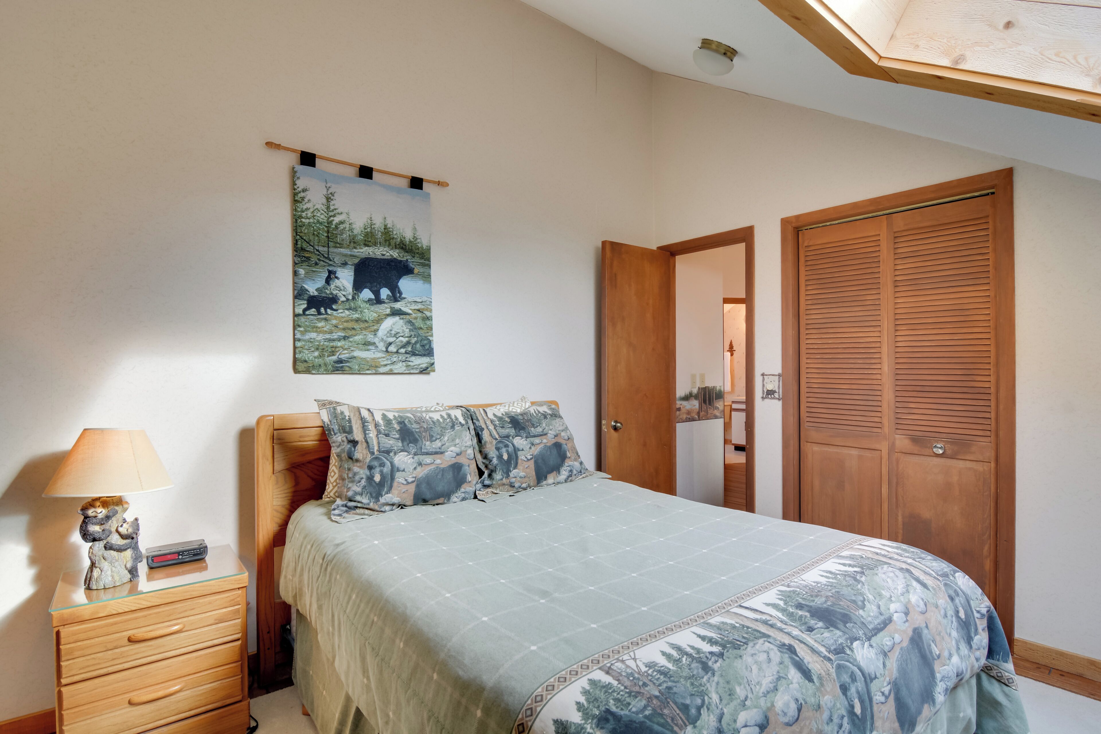 A bedroom with a bed, a nightstand, a lamp, a poster, and a wooden wardrobe.