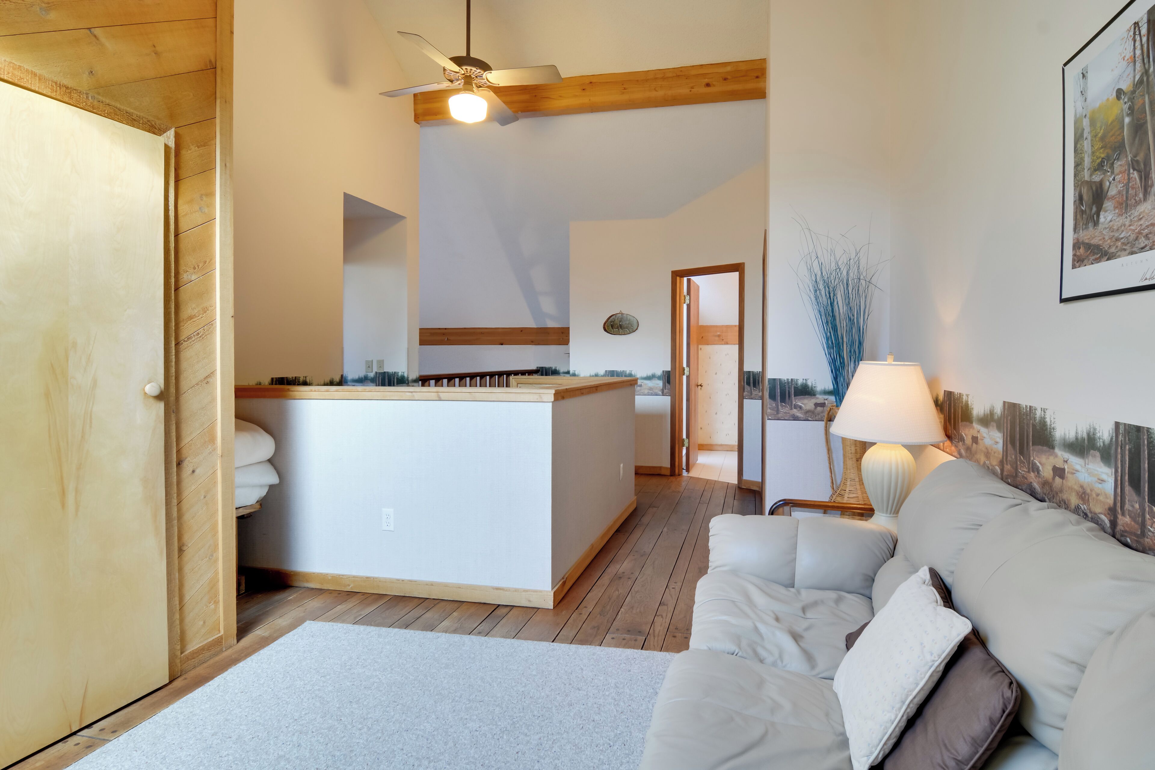 A cozy room with a wooden ceiling, a white sofa, a small table, and a painting on the wall.