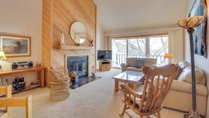 A cozy living room with a fireplace, wooden furniture, a television, and a large window.
