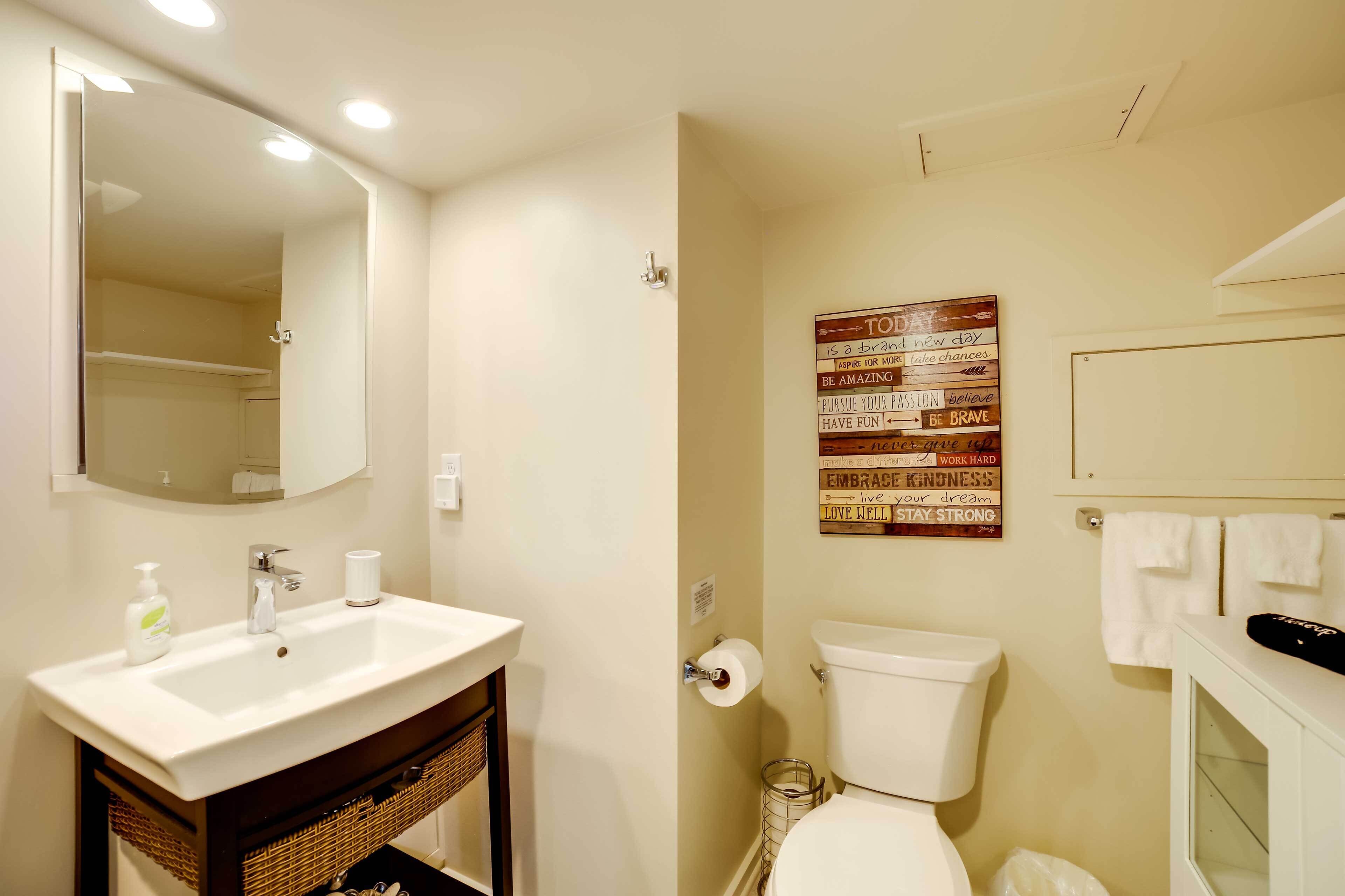 A bathroom with a white sink, mirror, and toilet. There is a motivational poster on the wall and a towel rack above the toilet.