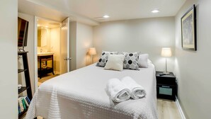 Cama bem arrumada com um edredom branco acolchoado, duas luminárias de cabeceira e um quadro na parede.