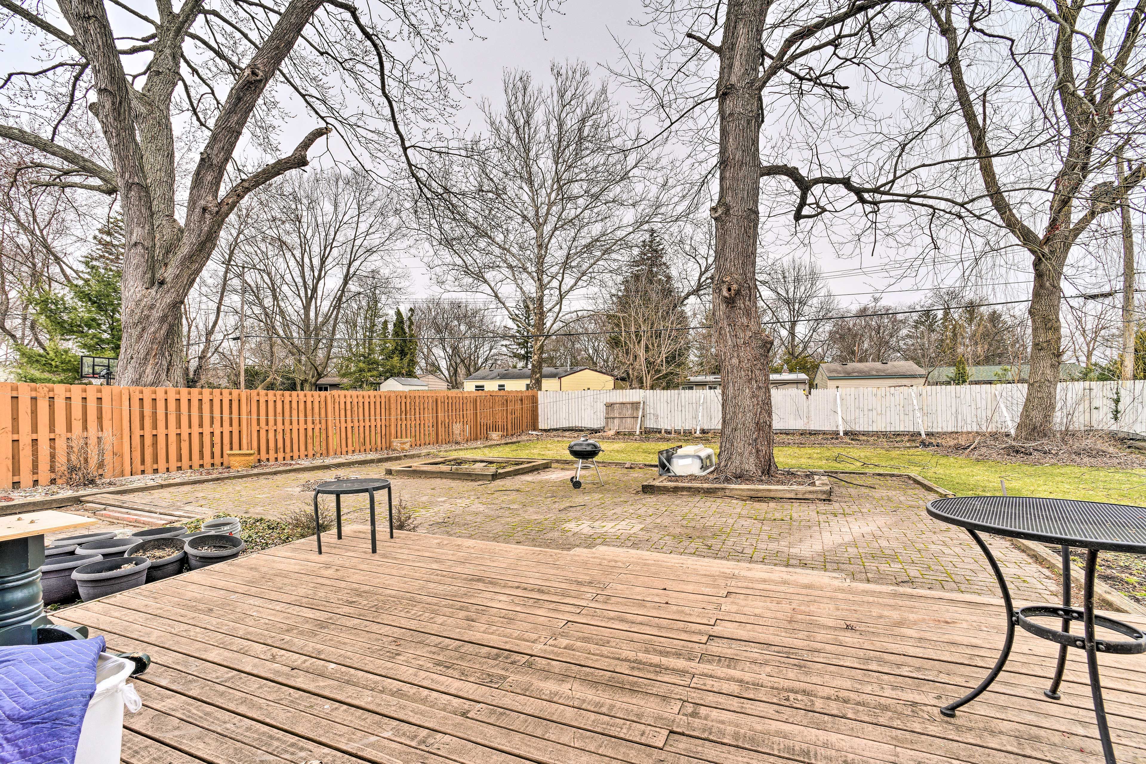 A wooden deck with a grill and a table, surrounded by trees and a wooden fence.