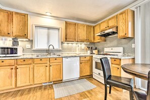 A modern kitchen with wooden cabinets, a dishwasher, a stove, and a dining area with a table and chairs. - Ann Arbor Home: 3 Mi to Stadium & Yost Ice Arena (Ann Arbor)
