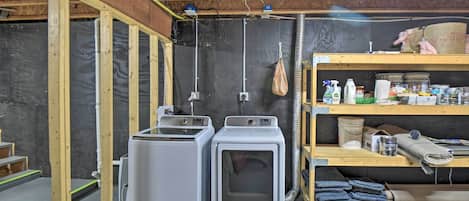 A laundry room with two stacked washing machines, a shelf with cleaning supplies, and a wooden bench.