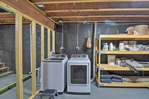 A laundry room with two stacked washing machines, a shelf with cleaning supplies, and a wooden bench. - Waterfront Lakes Region Home on Private Cove! (New Durham)