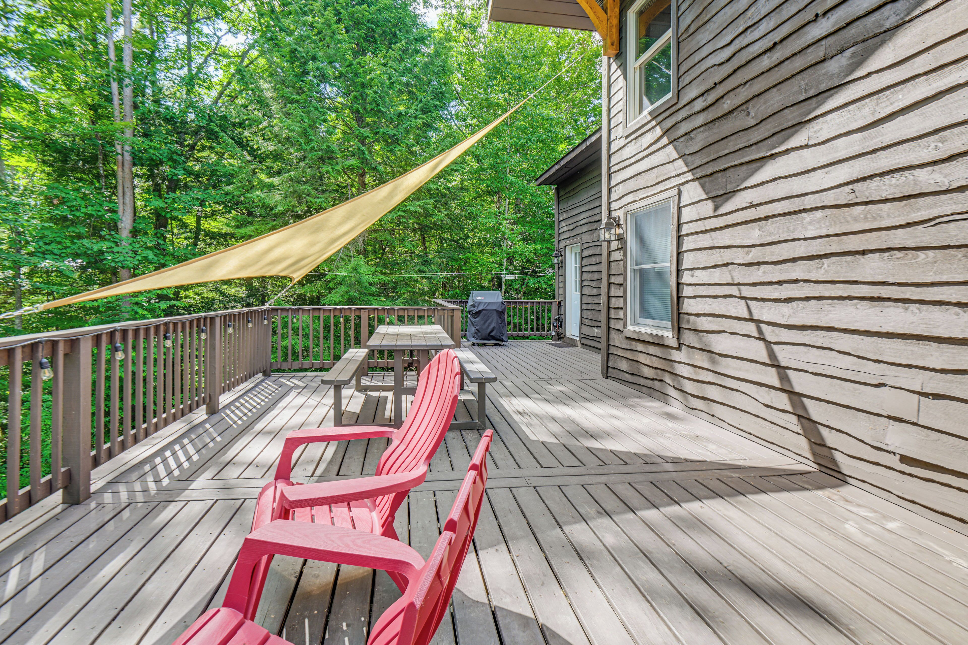 Une terrasse en bois avec des chaises rouges et une table, entourée d’une balustrade en bois et d’un auvent de couleur beige.