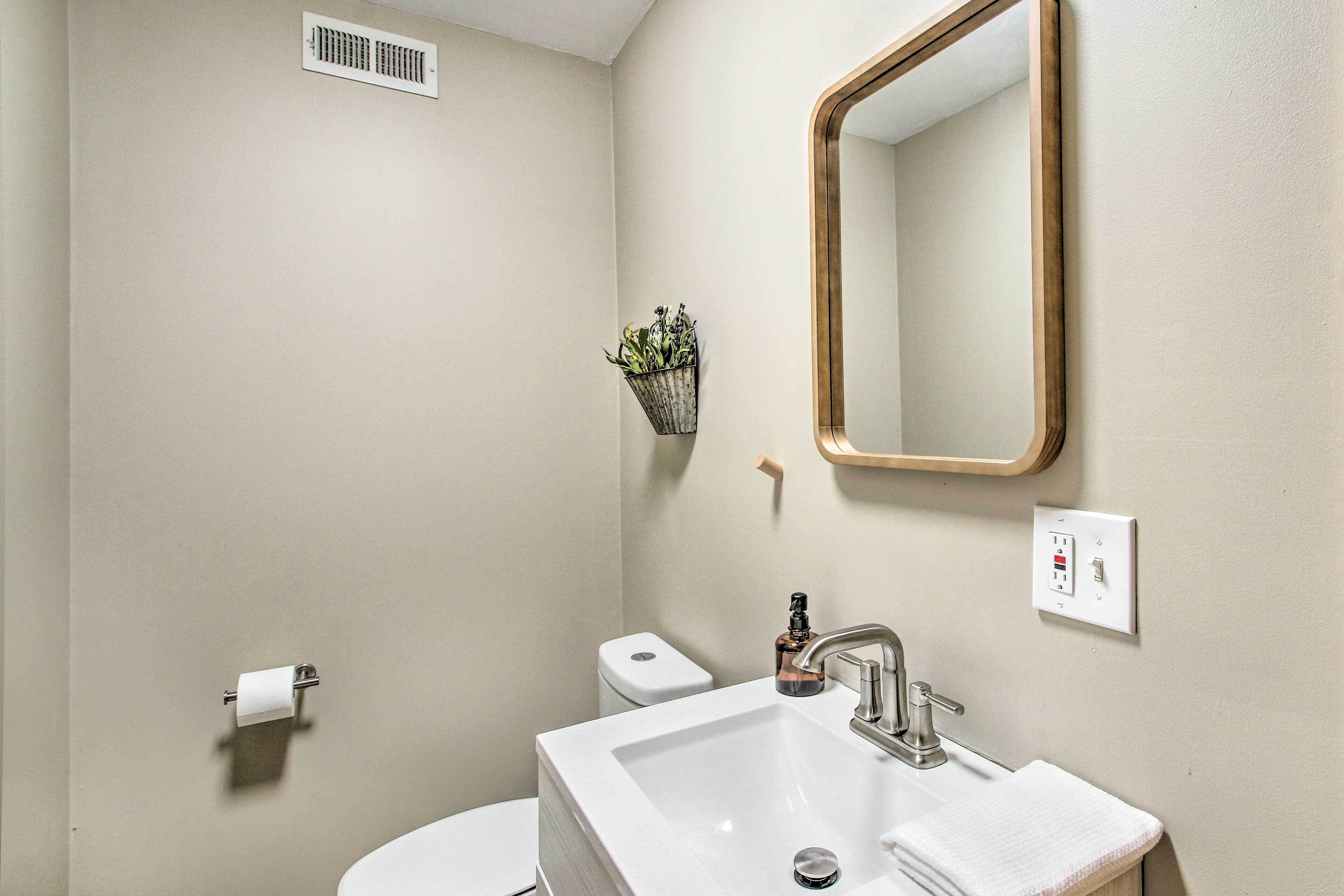 Een badkamer met een witte wastafel, een spiegel, een toilet en een kleine plant aan de muur.