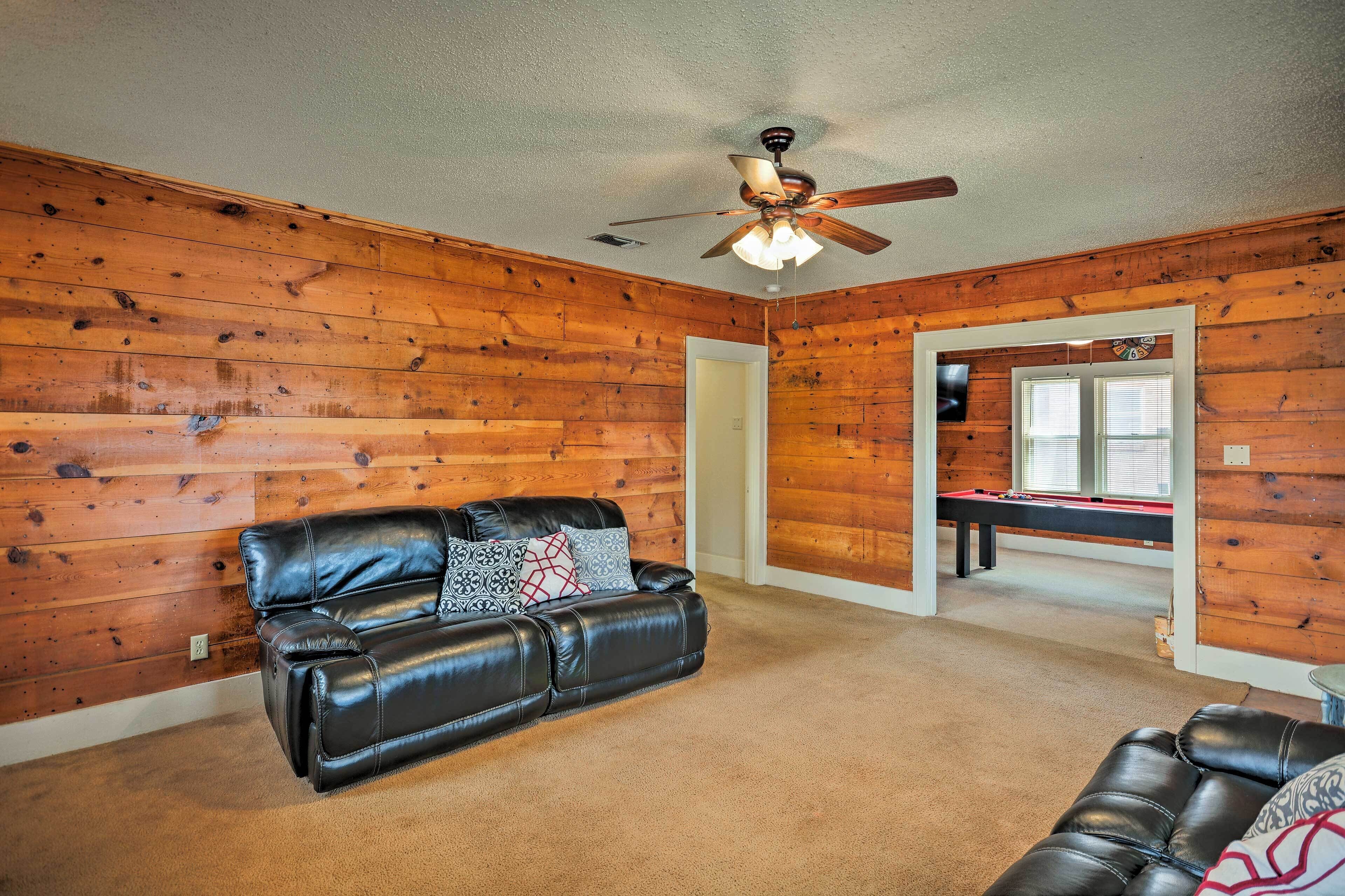 A room with wooden walls, a ceiling fan, a pool table, and a leather sofa.