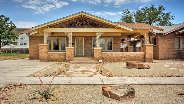 A two-story brick building with a covered porch, a stone pathway, and a landscaped garden with rocks and plants. - Inviting Lubbock Home > 1 Mi to Downtown (Lubbock)