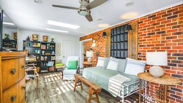 A room with a brick wall, a bed with pillows, a bench, a chair, a bookshelf, and a ceiling fan.