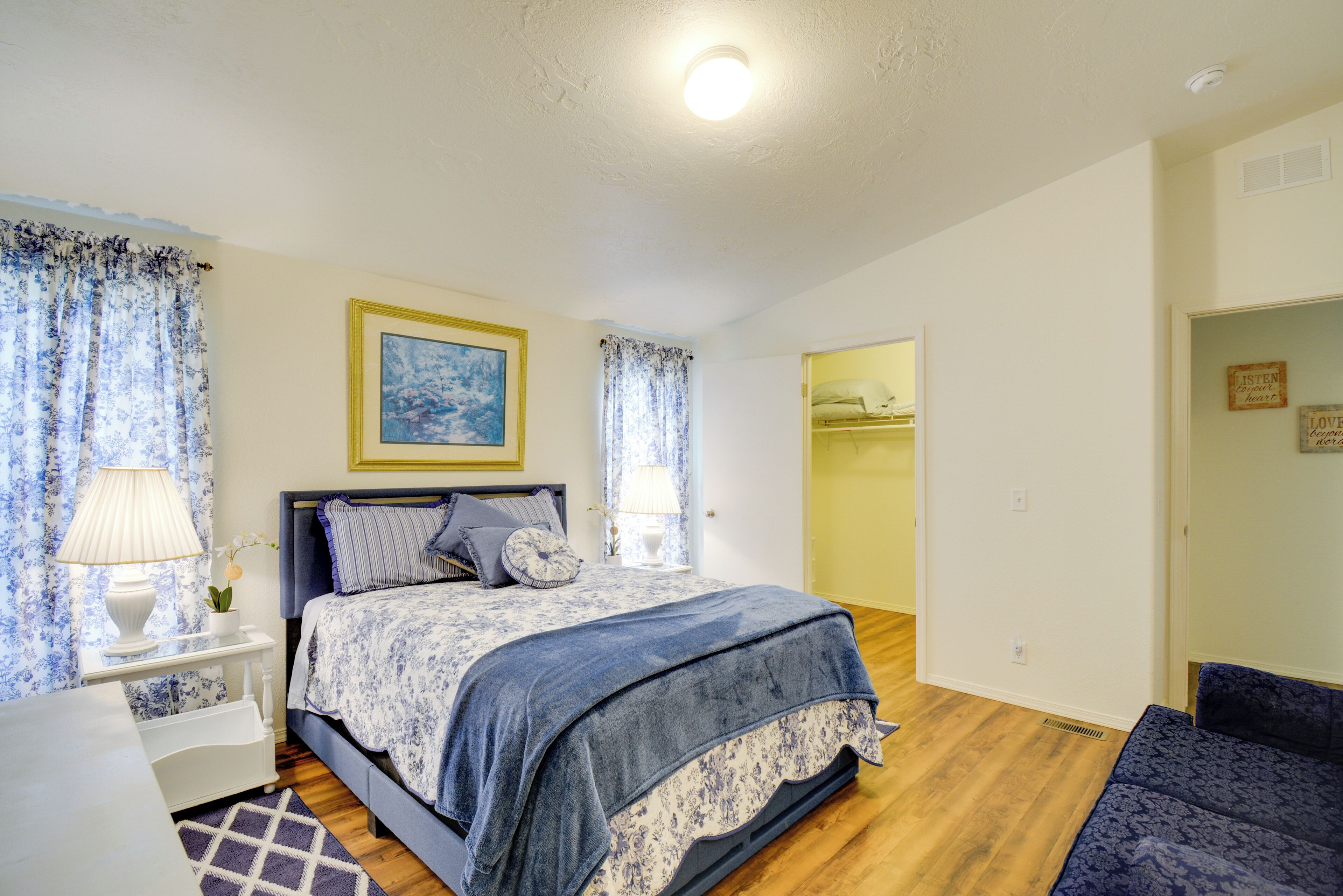 A bedroom with a bed, a nightstand, a lamp, a window with curtains, and a door leading to a closet.