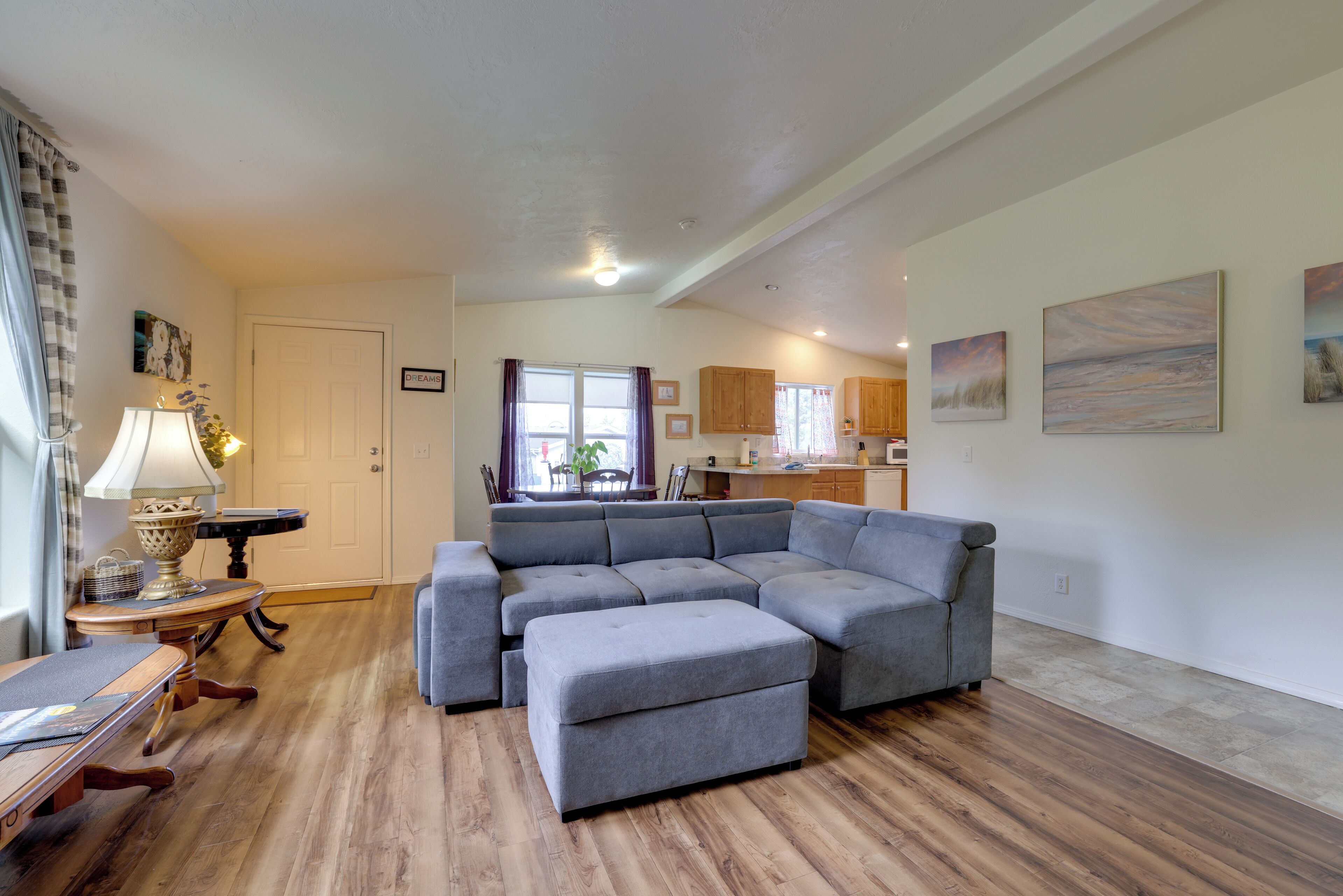 Un salon moderne avec un canapé d’angle, un pouf et une table à manger avec des chaises.