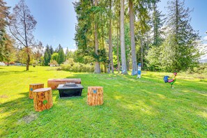 A grassy outdoor area with wooden benches and a fire pit. - Fire Pit + Patio: Peaceful Port Angeles Escape! (Port Angeles)