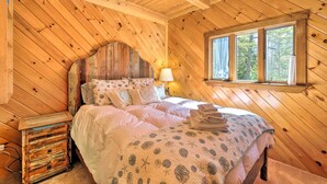 A wooden cabin bedroom with a bed, pillows, a nightstand, and a window. - Boothbay Harbor Cabin w/ Spacious Deck & Yard! (Boothbay Harbor)