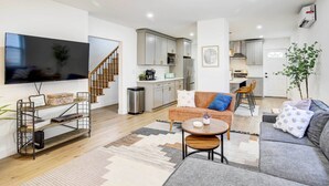 A modern living room with a sofa, coffee table, and TV. There is a staircase leading to a kitchen area. - Hudson Valley Vacation Rental: Near Hiking (Beacon)