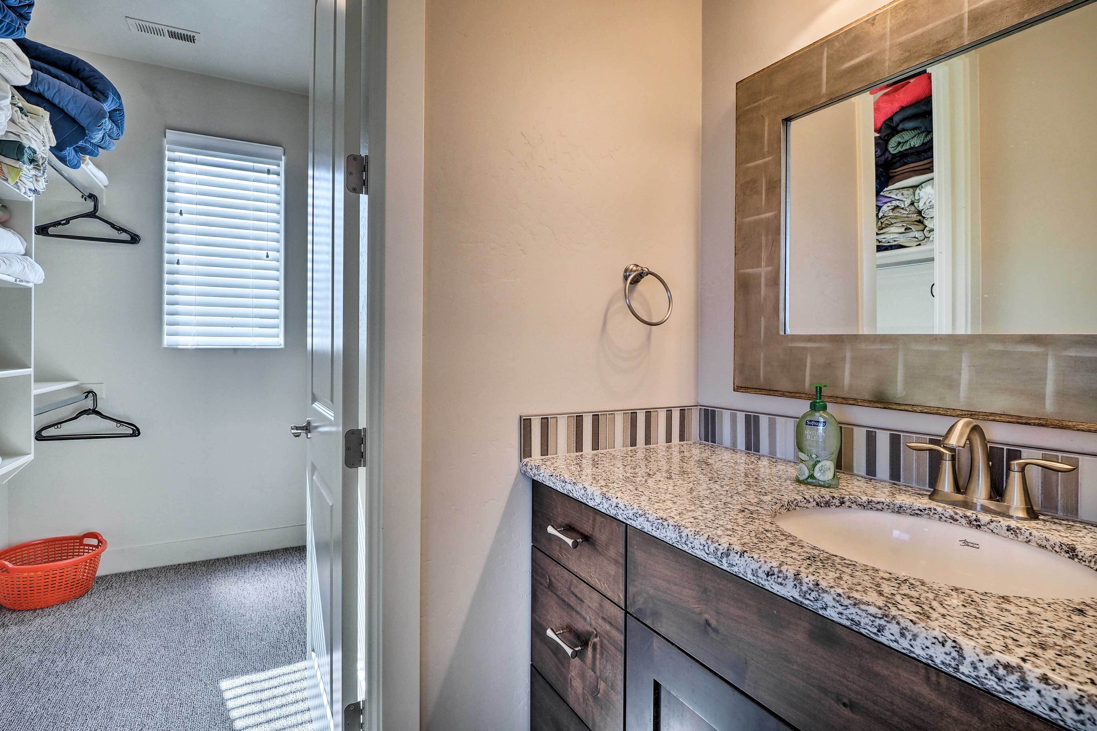 A bathroom with a granite countertop sink, a gold faucet, and a mirror above it. There is a towel rack on the wall and a basket on the floor.
