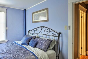 A bedroom with a bed, a framed picture on the wall, and a door leading to another room.