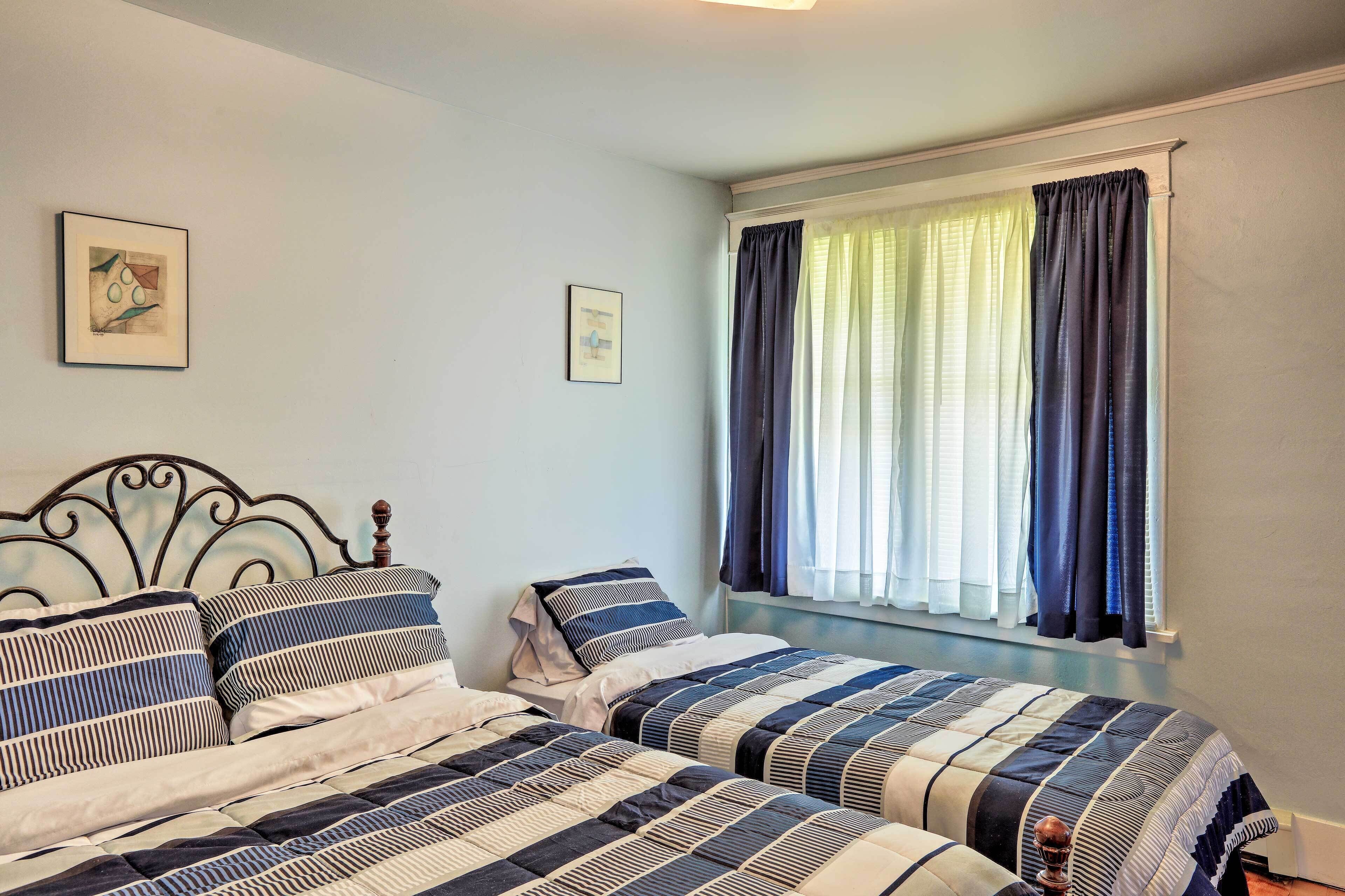 A bedroom with two beds, a window with curtains, and two framed pictures on the wall.