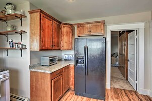 A kitchen with wooden cabinets, a stainless steel refrigerator, a toaster, and a countertop with shelves holding kitchen items.