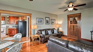 A living room with a leather sofa, a dining table with chairs, a ceiling fan, and a kitchen area visible through an open doorway. - Wyoming Farmhouse Retreat! 10 Mi to Bighorn Canyon (Lovell)
