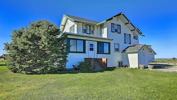 A two-story house with a green door and windows, a small attached garage, and a large tree in the front yard.