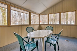 A room with a round table and four chairs, large windows with a view of trees, and wooden panel walls. - Cozy Lake Ariel Home w/ Community Amenities! (Lake Ariel)