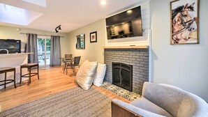 A modern living room with a fireplace, a dining area, and a kitchen visible through a glass door. - Updated Home w/ Pool + Deck ~ 2 Mi to Dtwn! (Saratoga Springs)