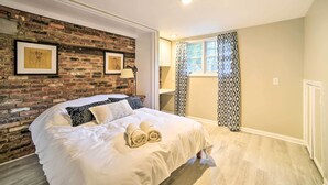 A neatly made bed with rolled towels, a brick wall with framed artwork, and a window with patterned curtains. - Updated Home w/ Pool + Deck ~ 2 Mi to Dtwn! (Saratoga Springs)