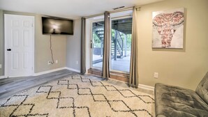 A room with a large window, a flat-screen TV mounted on the wall, a patterned rug, and a gray sofa. - Updated Home w/ Pool + Deck ~ 2 Mi to Dtwn! (Saratoga Springs)