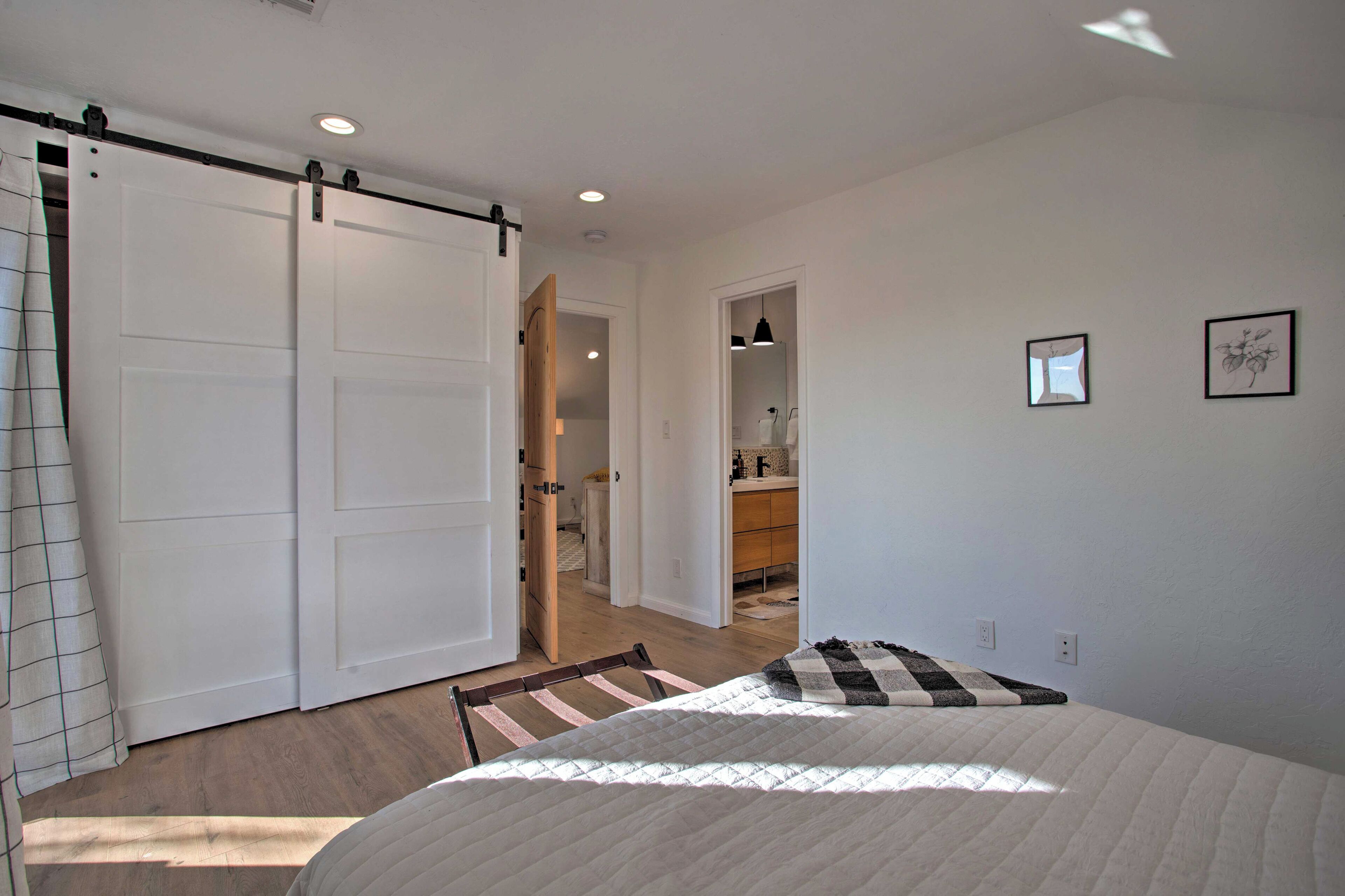 A bedroom with a bed, a sliding door, a bathroom, and a hallway.