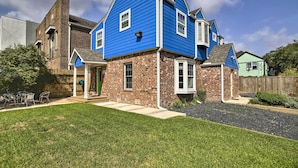 Uma casa de dois andares com fachada de tijolos e revestimento azul, varanda frontal e gramado bem cuidado.