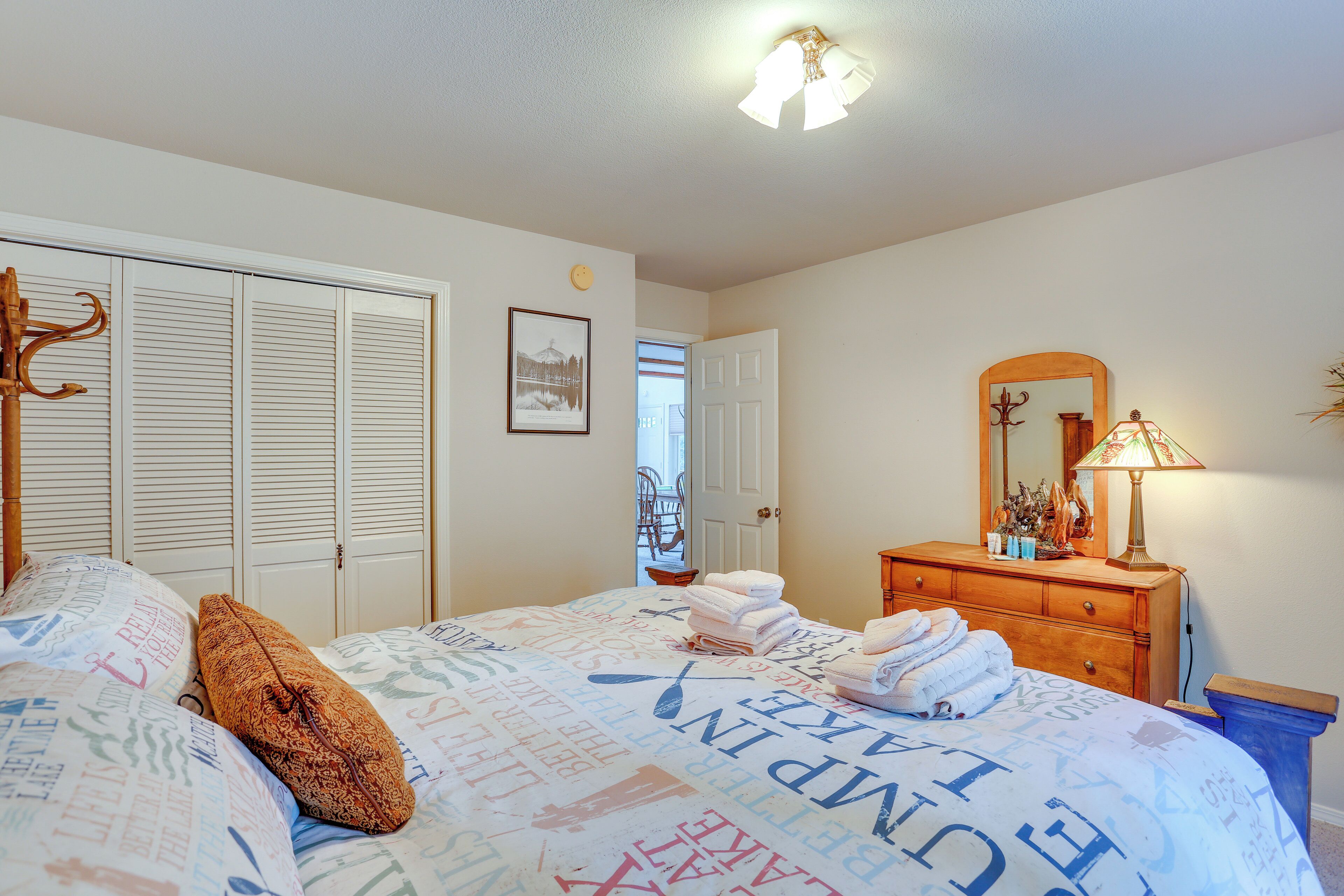 A bedroom with a bed, a dresser, a mirror, and a door leading to another room.