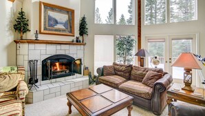 A cozy living room with a fireplace, a large window, and a view of trees. - Pet-friendly California Cabin w/ Beach Access (Chester)